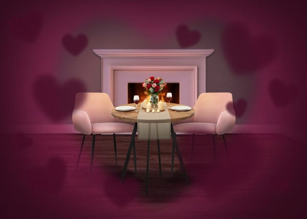 Romantic dining setup with a small round table set for two, pink upholstered chairs, candles and a bouquet of roses, placed in front of a lit fireplace, with soft heart-shaped overlays creating a Valentine&rsquo;s Day atmosphere.