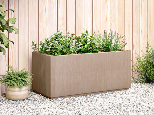 Large planter filled with plants and smaller potted plant, on gravel ground against a wooden fence. Click to see the products in the collection.