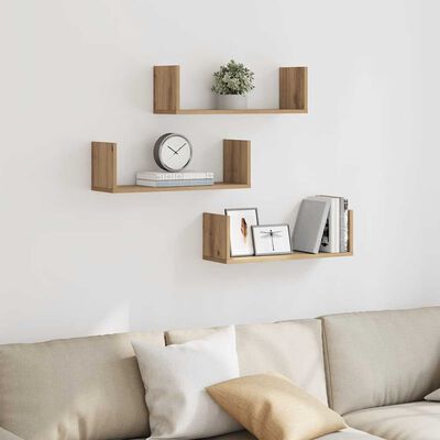 Three wooden wall shelves mounted on a white wall with a sofa below; decor like clock, books, and photos on the shelves.