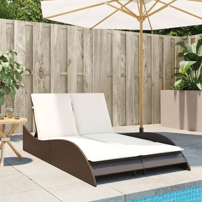 Wicker outdoor daybed with two cream cushions and umbrella in background