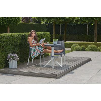 Person reading a book at a small outdoor table with chair set on a wooden deck.