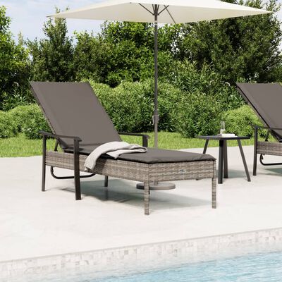 Outdoor lounge chair with dark gray cushion and matching wicker base, patio by a pool with another chaise and umbrella.