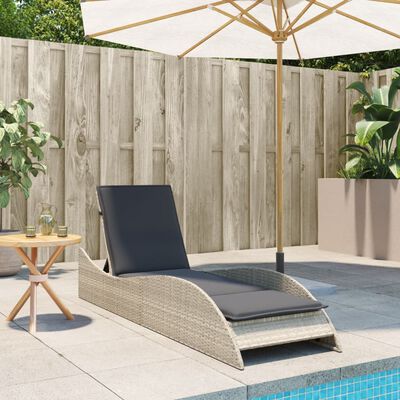 Rattan chaise lounge with dark cushions by pool area, with umbrella and planters.