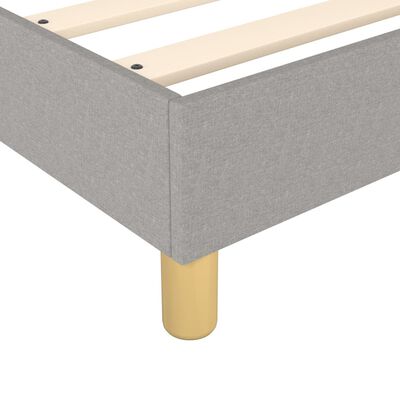Close-up of a rounded light wood leg of a grey upholstered bed frame